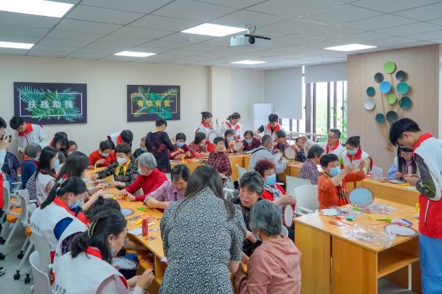 志愿者與殘障老人一起編織二十四節氣團扇。學校供圖